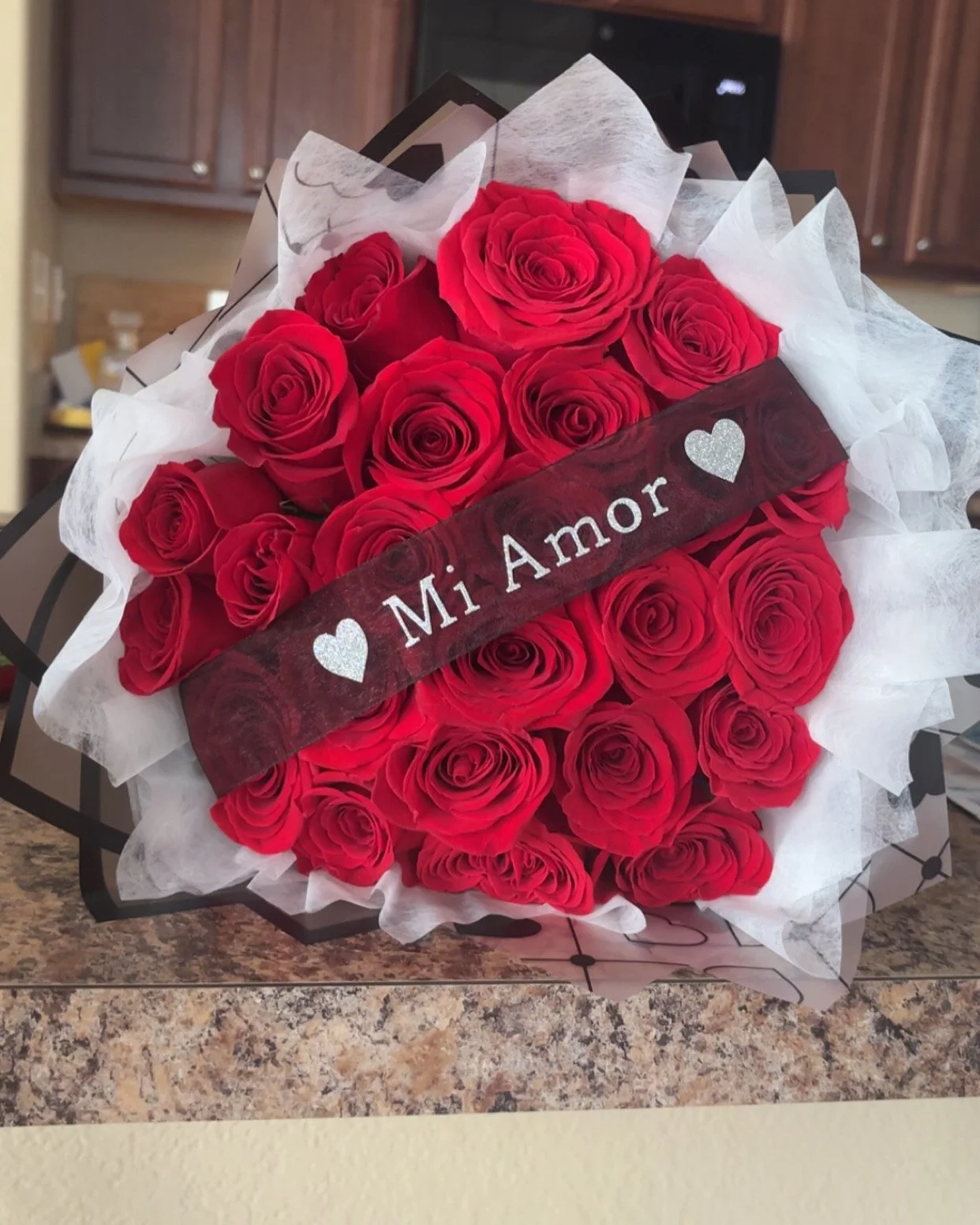 A bouquet of red roses wrapped in decorative paper, with a sign that reads 'Mi Amor' and hearts.