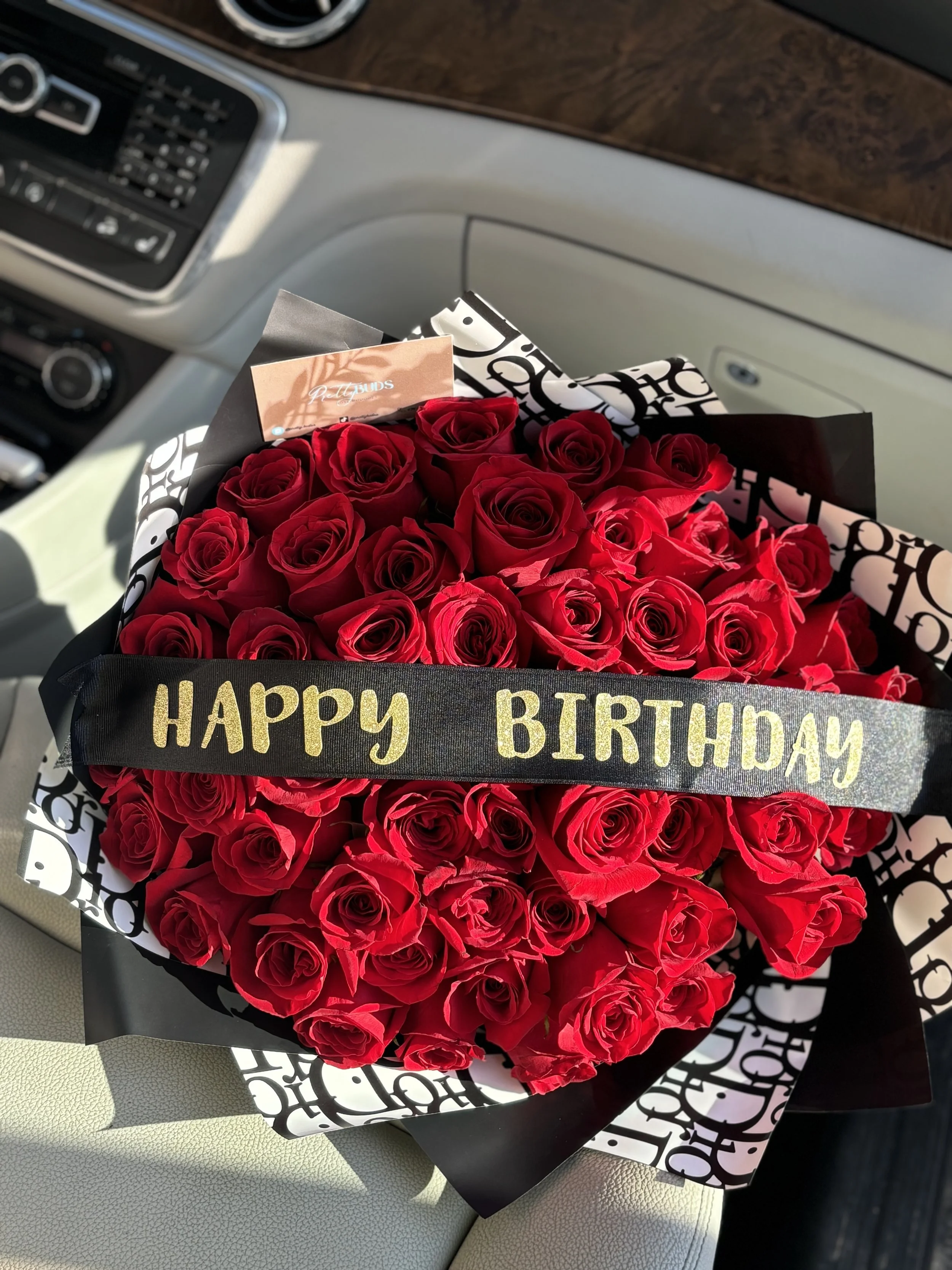 A bouquet of red roses with a black ribbon stating 'HAPPY BIRTHDAY' inside a car.
