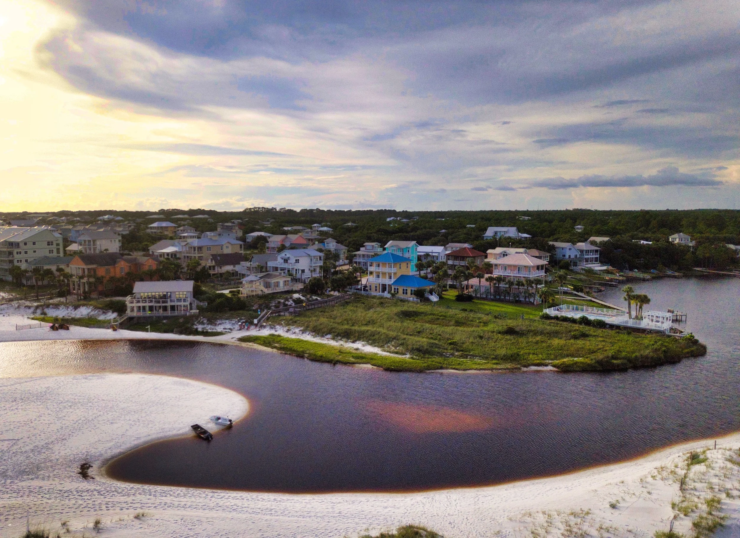 Aerial view of a coastal neighborhood with colorful houses along water with a sandy beach and boats