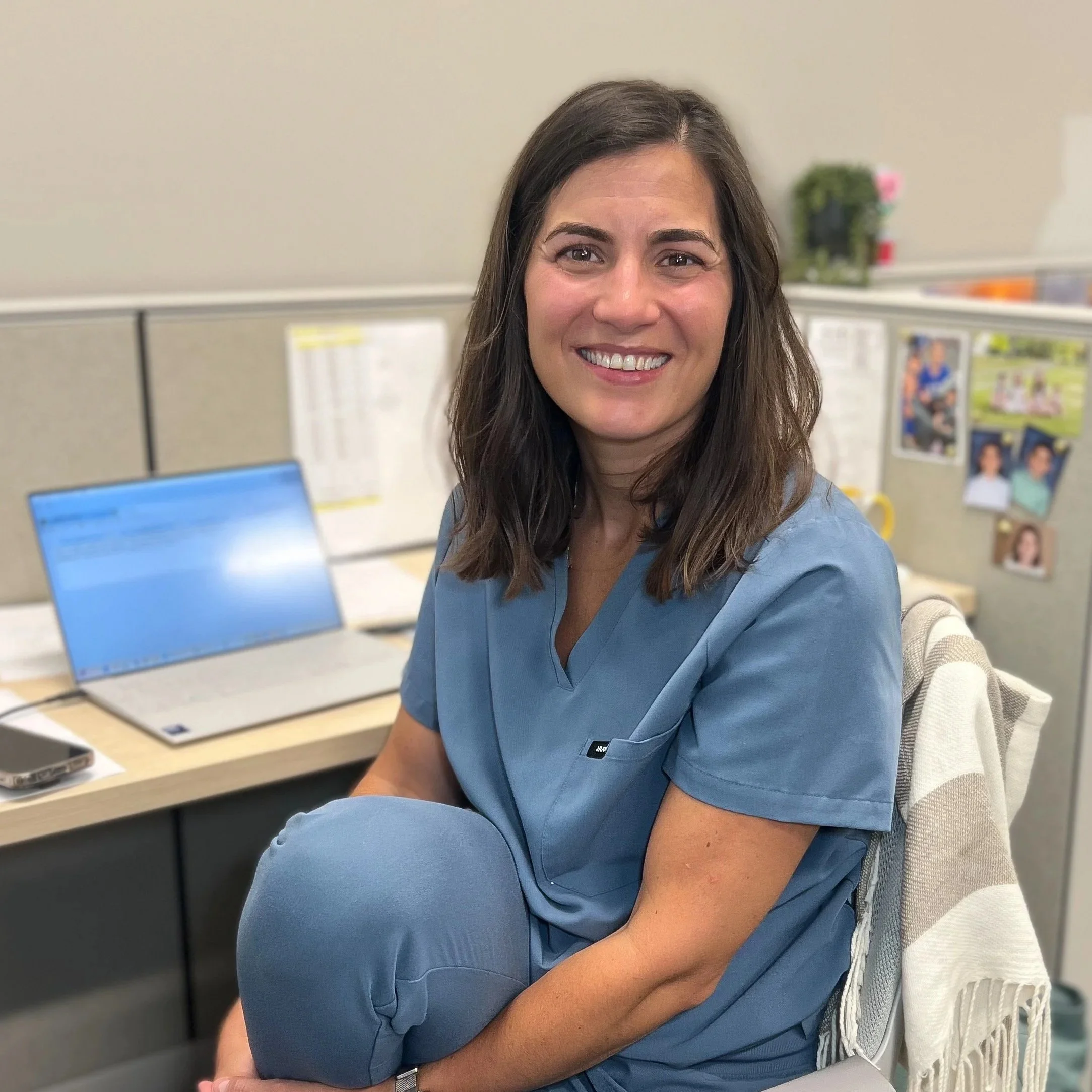 Female healthcare professional in blue scrubs sitting at her desk in an office.