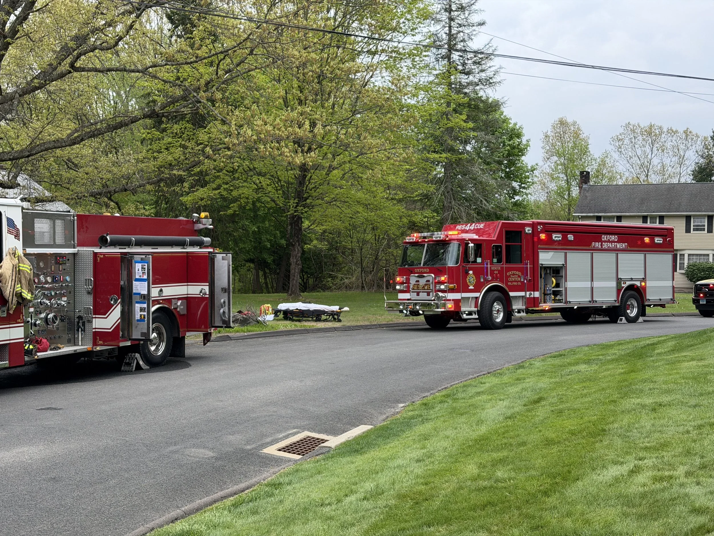 Fire trucks parked on the side of the street, with a suburban house and trees in the background.