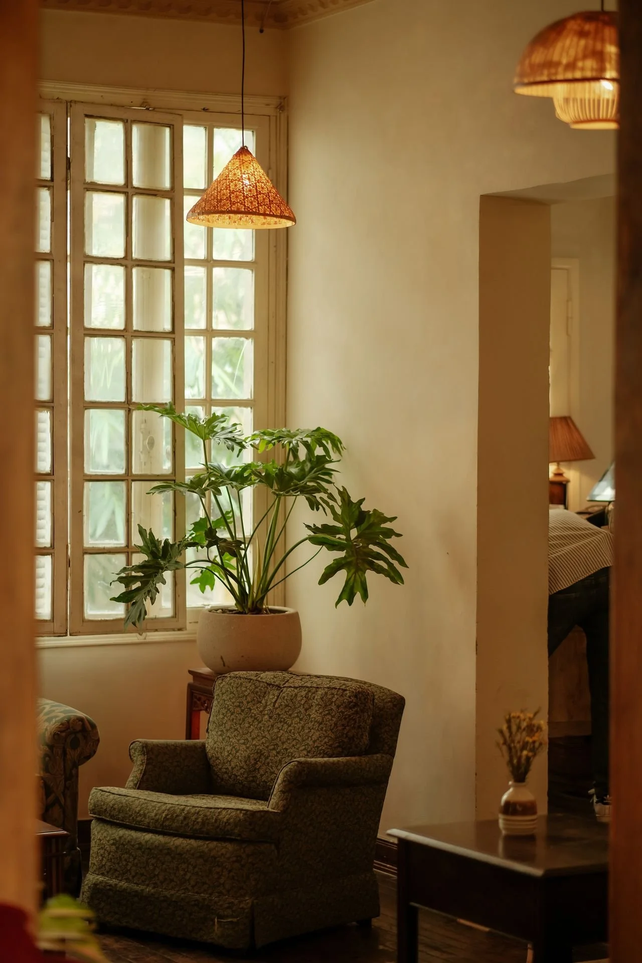 Living room with a green armchair, a potted plant by the window, a small table with a vase, and warm lighting.