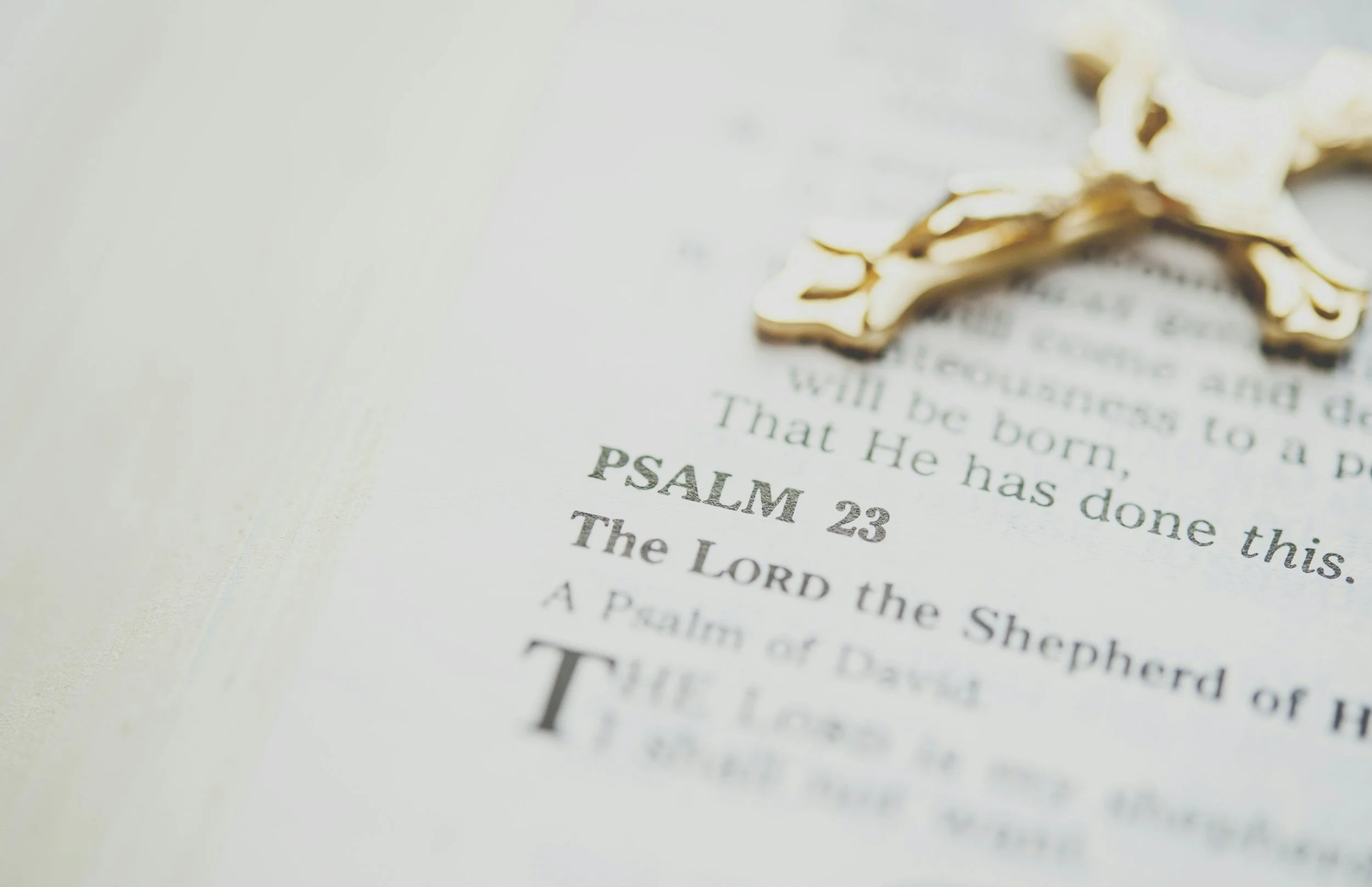 Close-up of a page in a Bible, highlighting Psalm 23, with a gold decorative embellishment at the top.