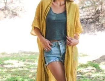 Person wearing a yellow shawl, blue t-shirt, and denim shorts standing outdoors.