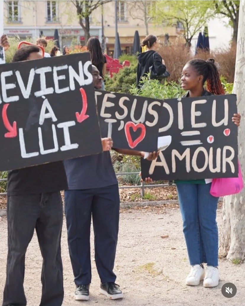 Deux personnes tiennent des panneaux en protestation ou en soutien, avec un parc ou une zone urbaine en arrière-plan.