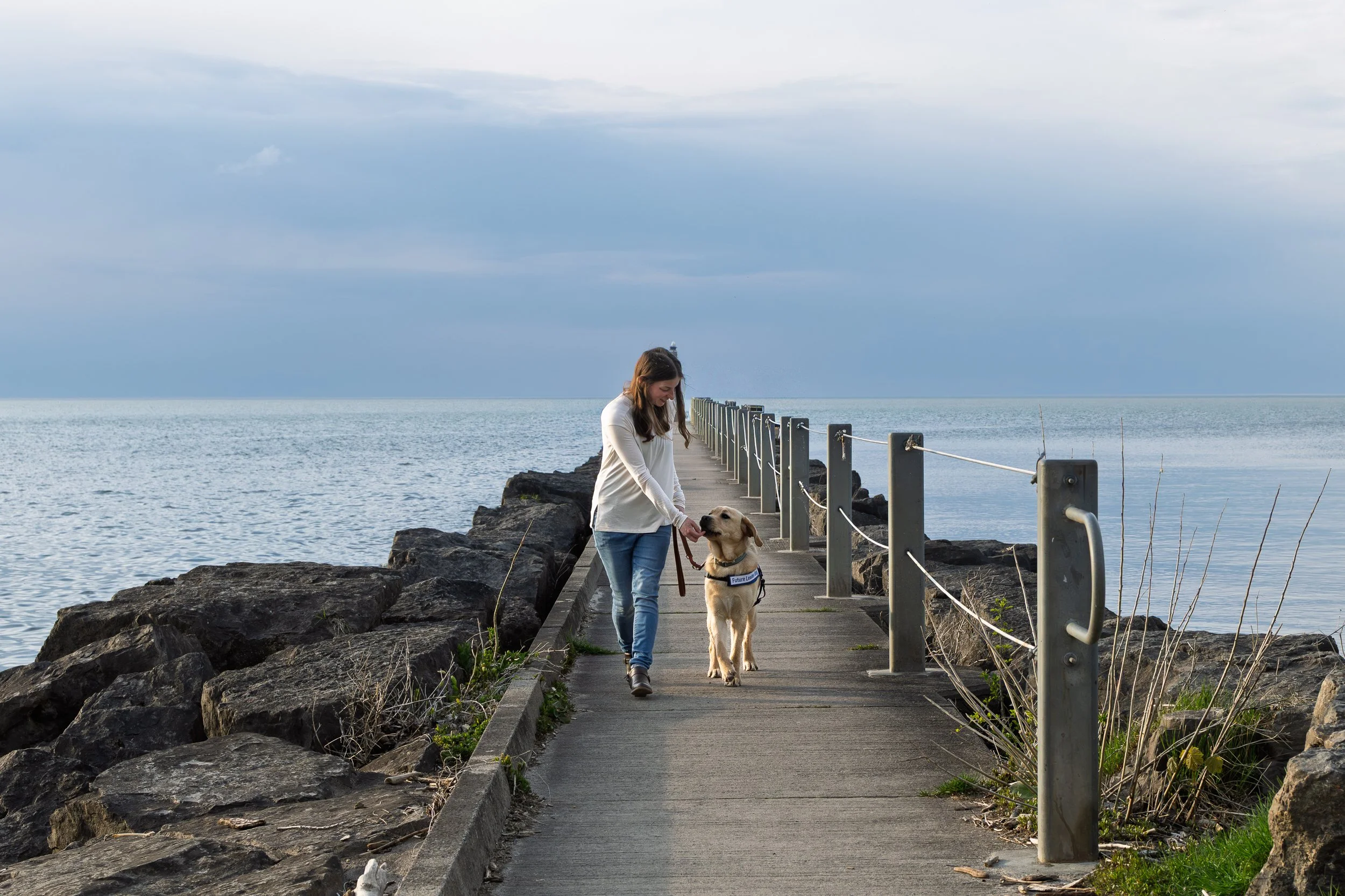 Puppy raiser walking a Future Leader Dog on the pier at Webster Park with Lake Ontario in the background, Webster NY