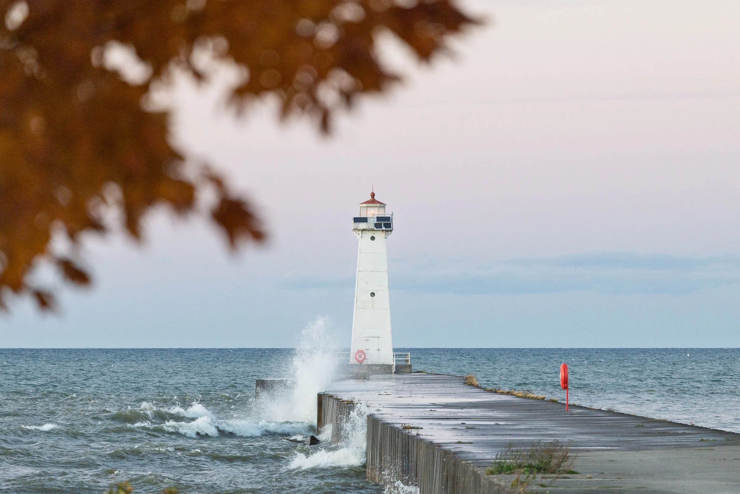 The Sodus Point lighthouse and pier on Lake Ontario in Wayne County, New York, with autumn foliage in the foreground at golden hour.