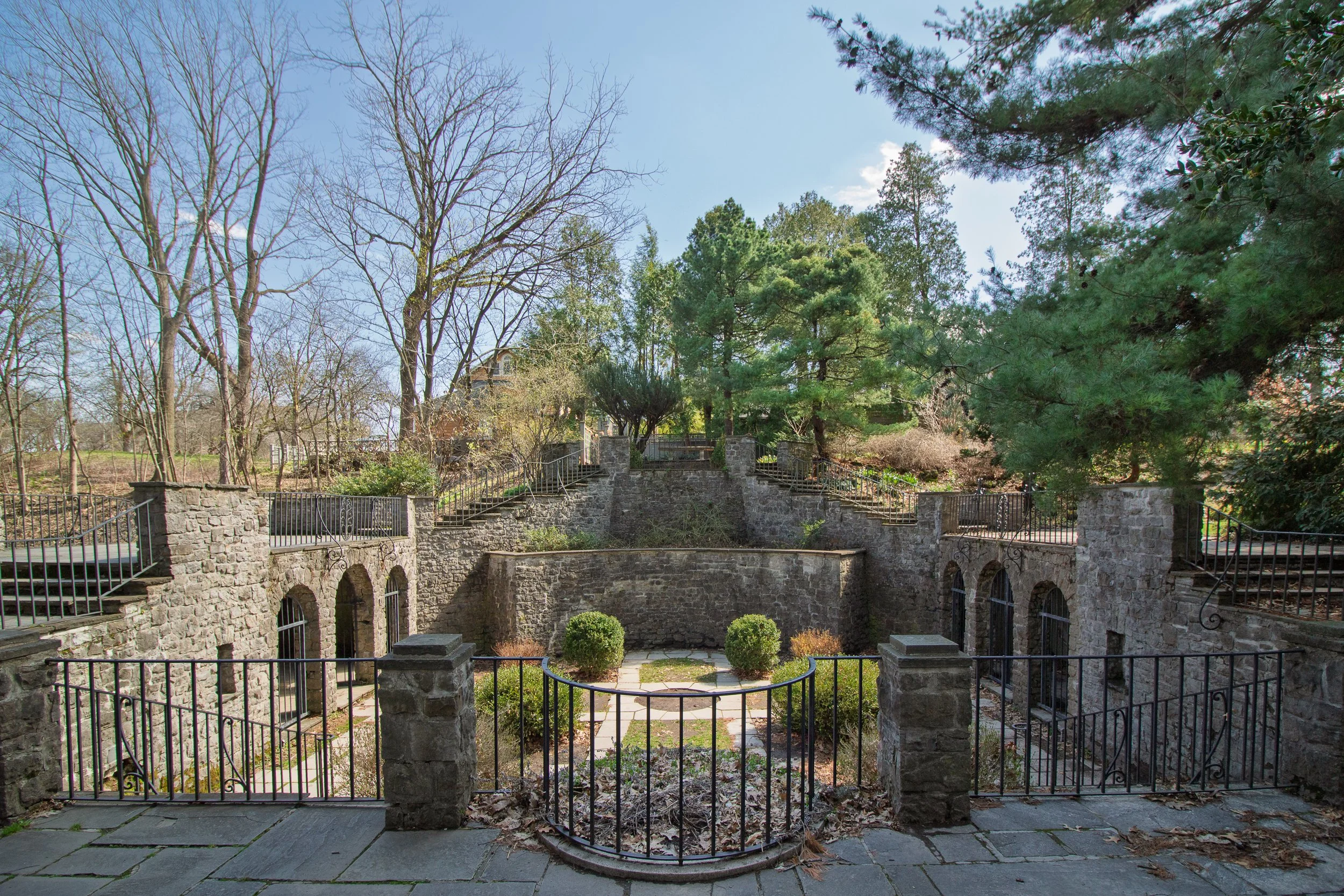 The terraced stone walls, arched niches, and ironwork railings of the Sunken Garden at Warner Castle in Highland Park, Rochester, NY, photographed in early spring before foliage fills in.
