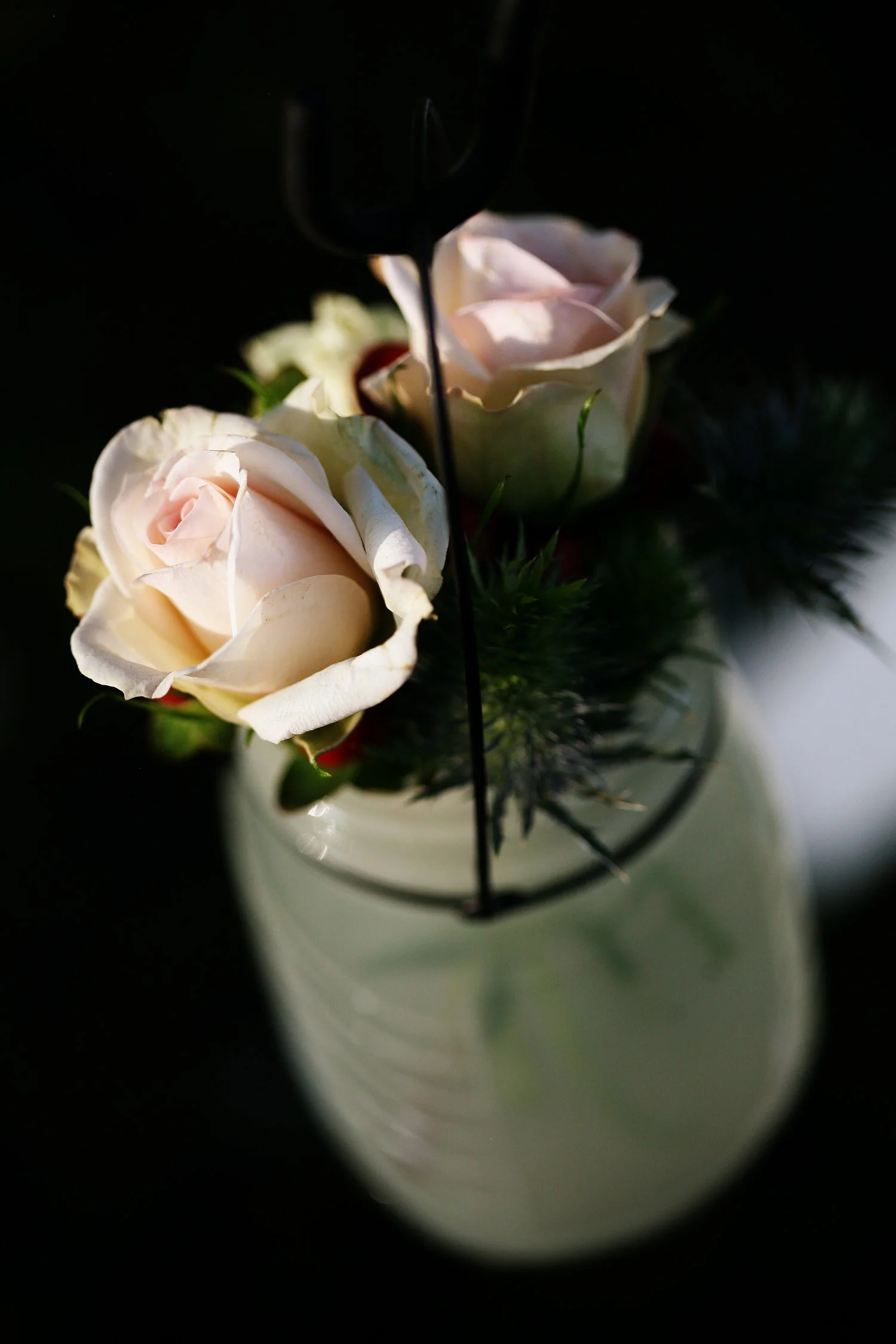 A white frosted mason jar holds two pale pink roses and some greenery. 