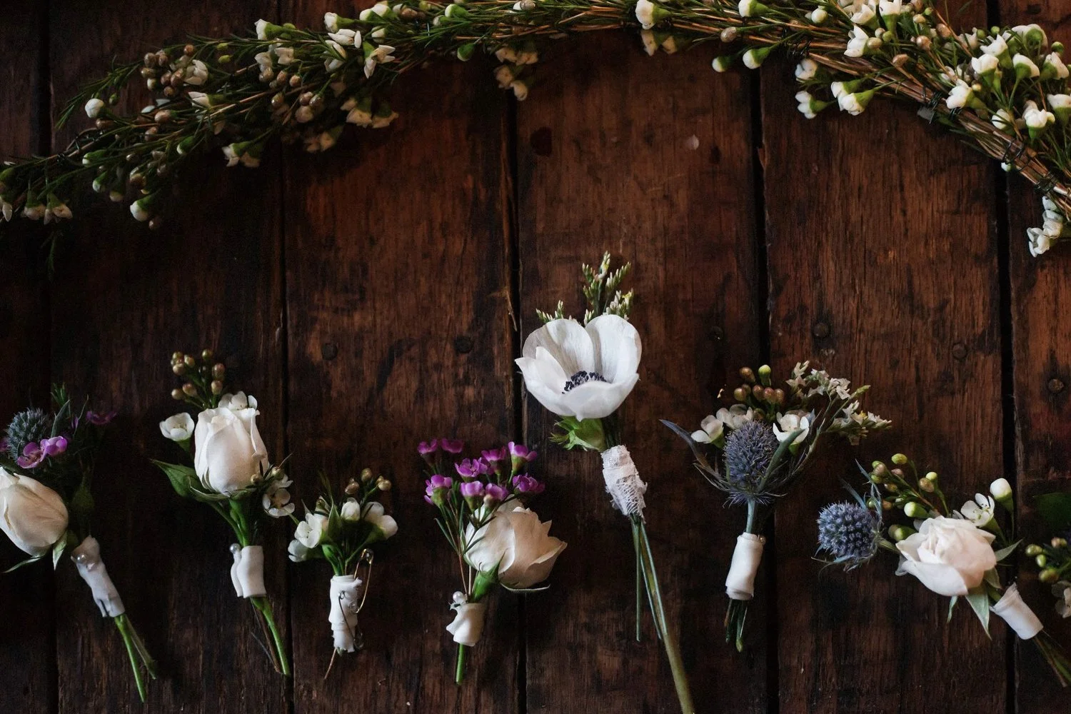 Boutonnieres for an outdoor Southern wedding arranged next to each other on a dark hardwood floor.