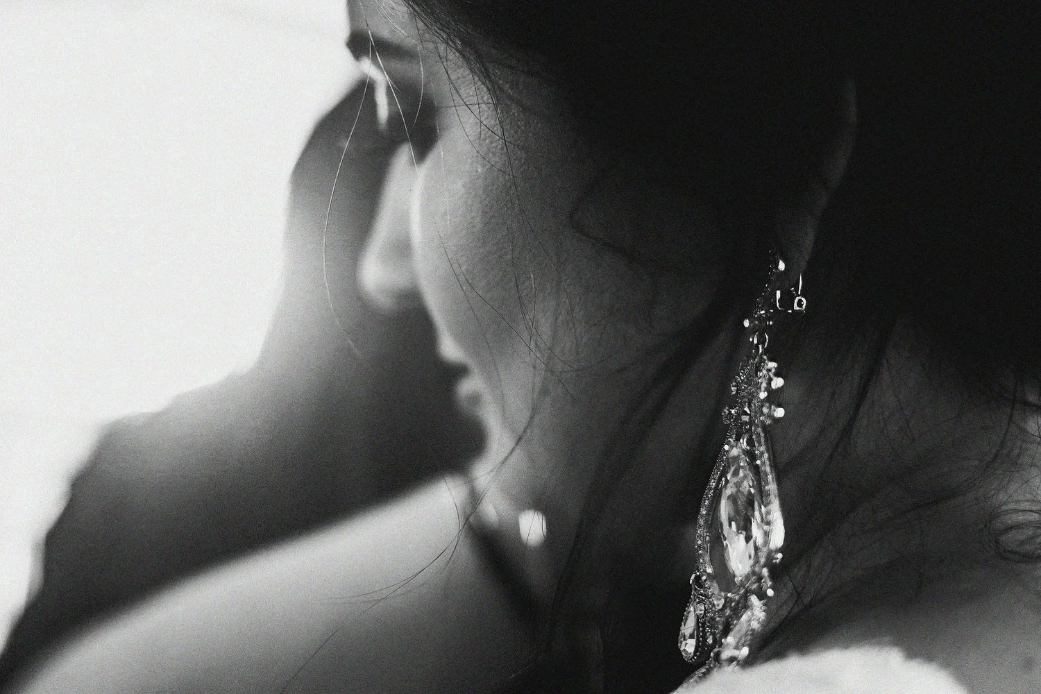 Window light comes in and hits a dangly silvery jeweled earring on a woman's ear. You can see her face looking toward the light.