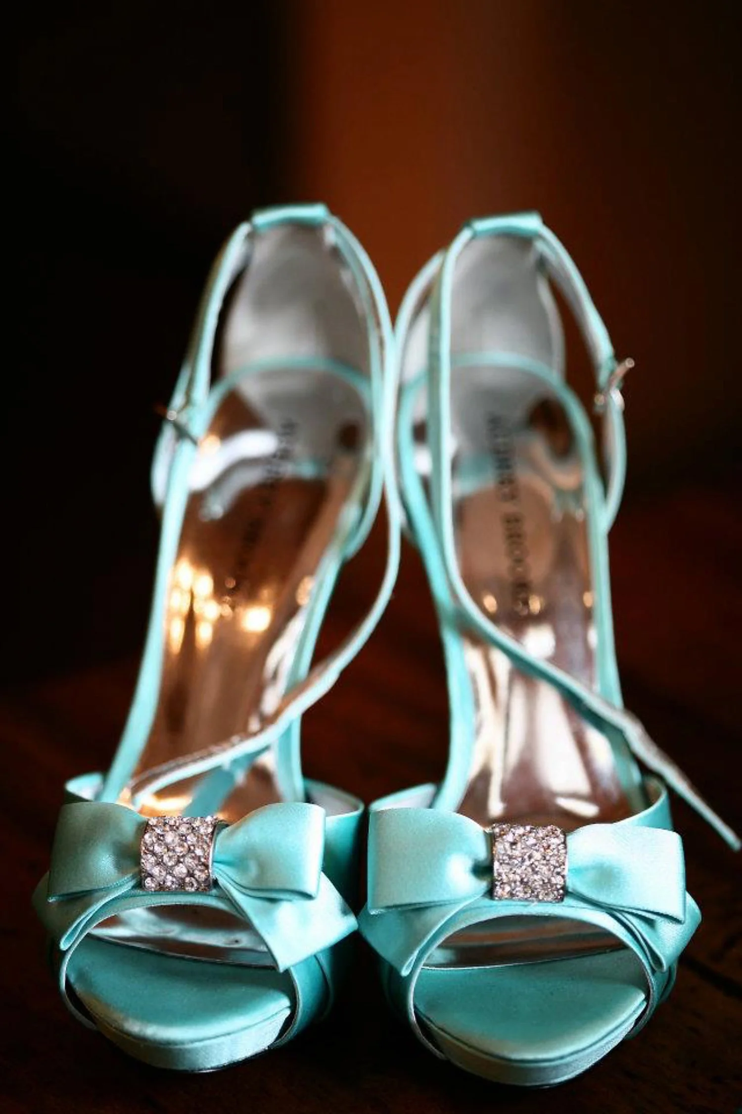 Tight vertical photograph of a pair of turquoise open-toe high heels with bows holding jewels in the center. 
