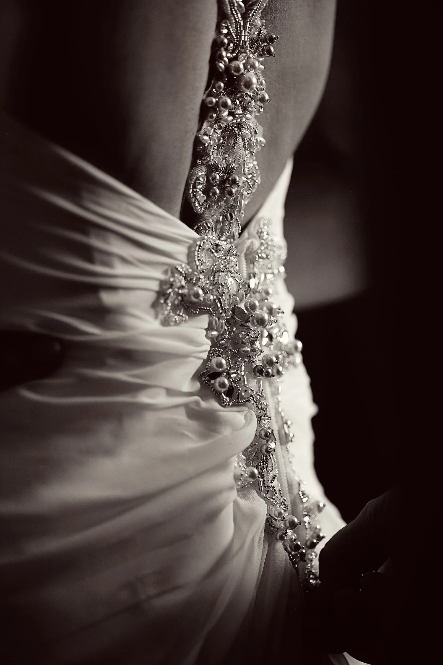 Close-up of a wedding dress with ornate beaded embellishments and ruching on the fabric, black and white photo.