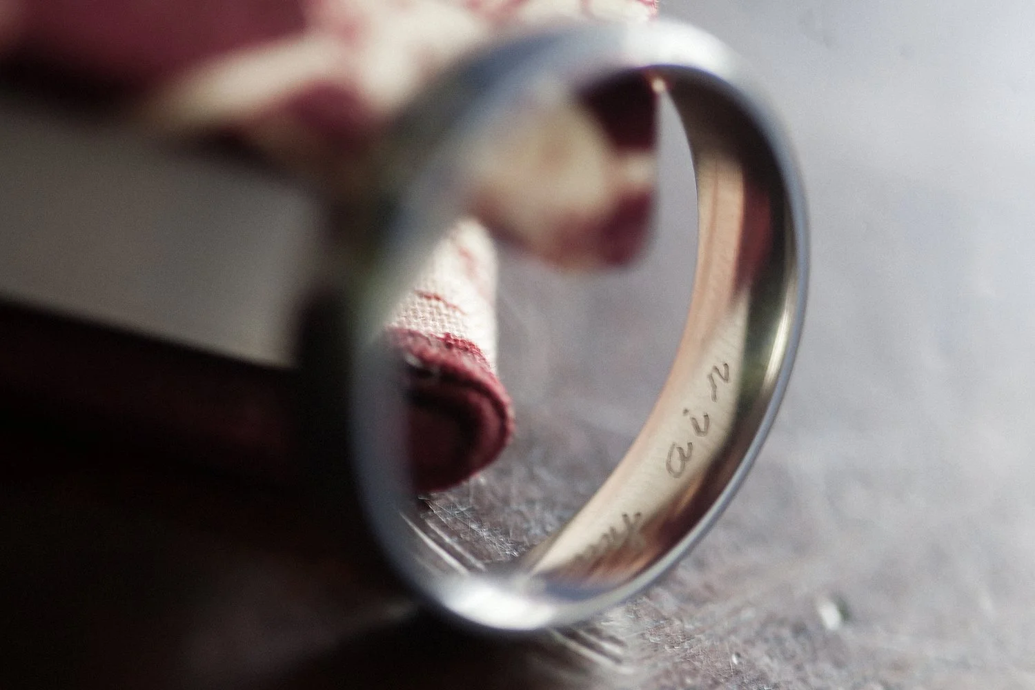 Macro shot of the inside of a white told wedding band sitting on a wooden surface. The inscription "my air" is visible on the interior of the band.