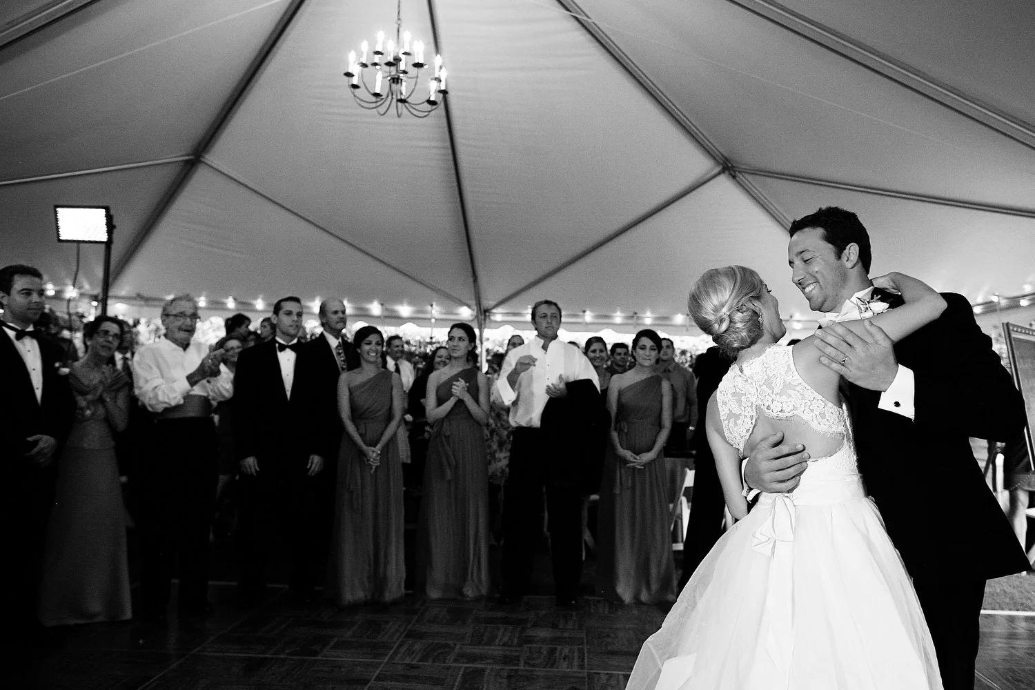 A bride and groom sharing a dance during their wedding reception inside a large tent, with guests watching and smiling.