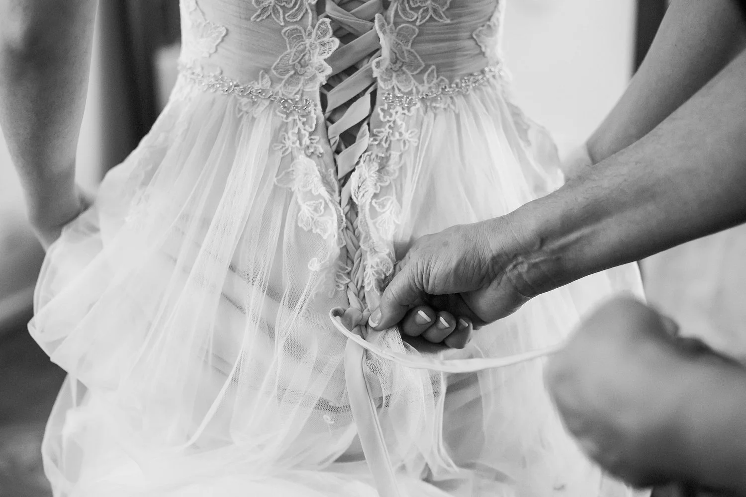 Close-up of someone lacing up a wedding dress with lace and fabric detailing.