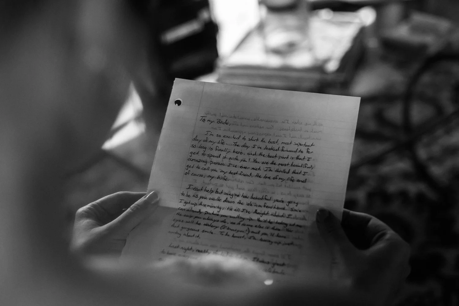 A person holding a handwritten letter, with a blurred background including books and a table.