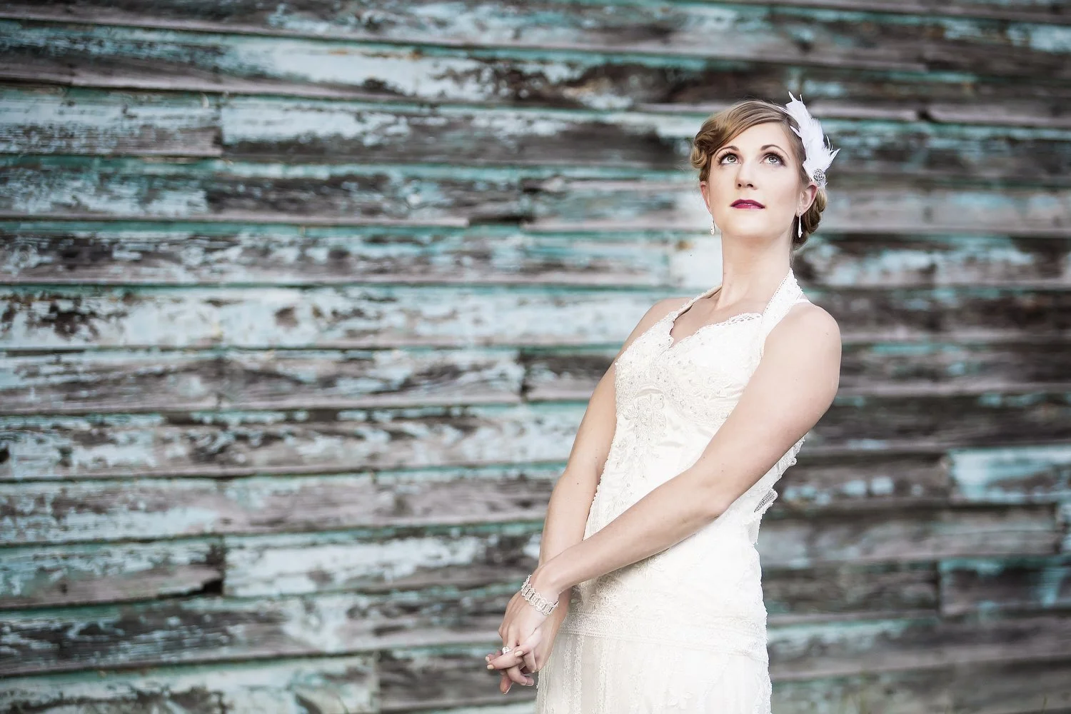 A woman in a white wedding dress standing in front of a weathered wooden wall with teal paint.