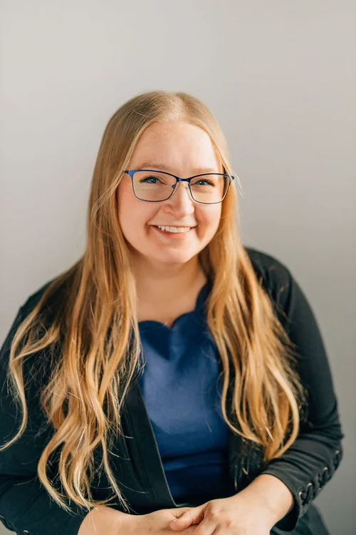 Shiree, smiling, wearing glasses and a dark cardigan