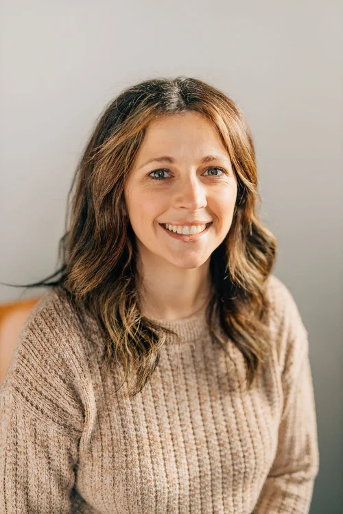 Maghen, smiling, wearing a beige knit sweater