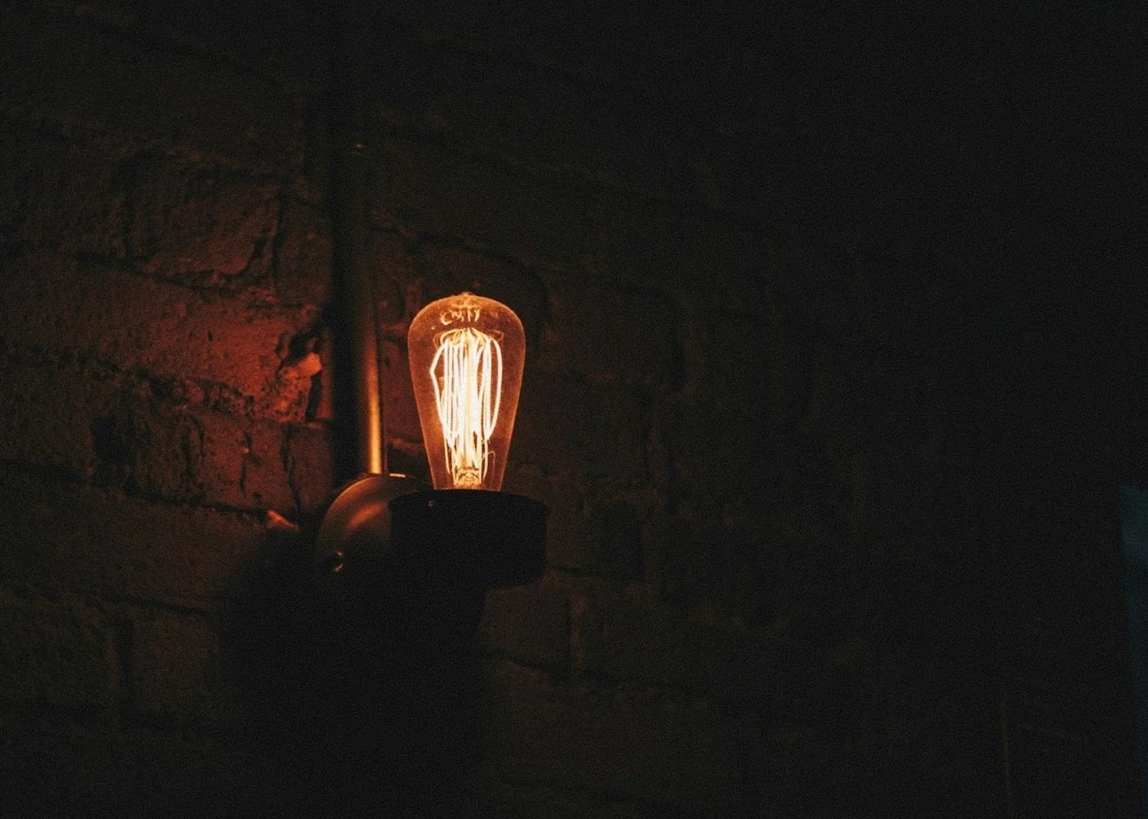 A vintage-style Edison light bulb glowing softly, mounted on a dark wall with exposed brick.