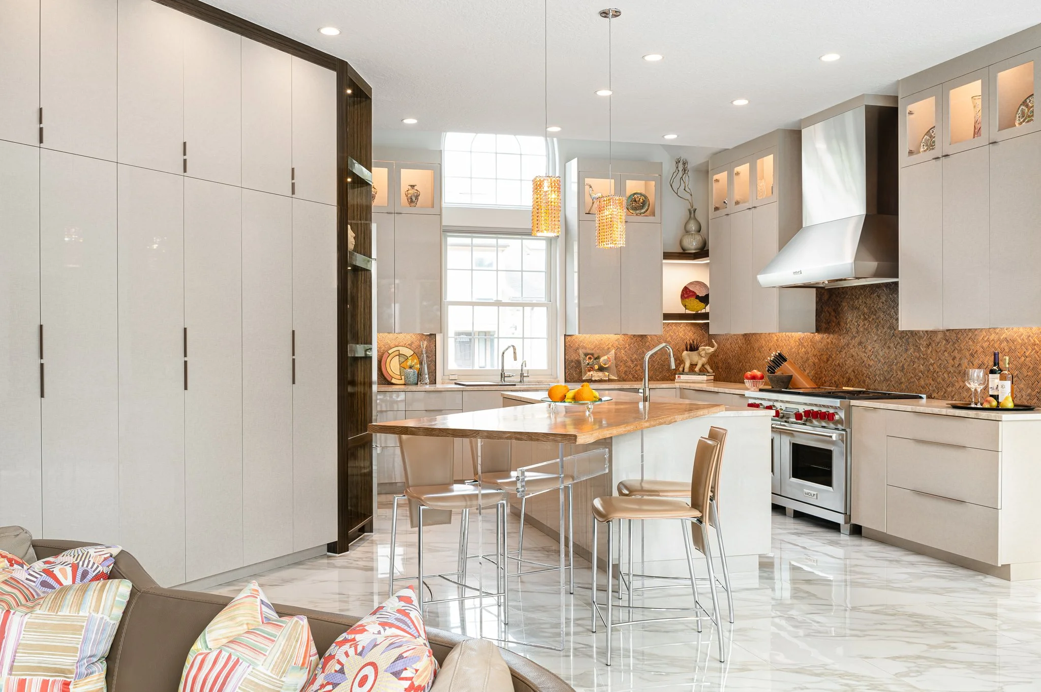 Modern kitchen with white cabinets, a marble tile floor, an island with a wooden countertop, and pendant lights. There are decorative items on the shelves and a window above the sink.