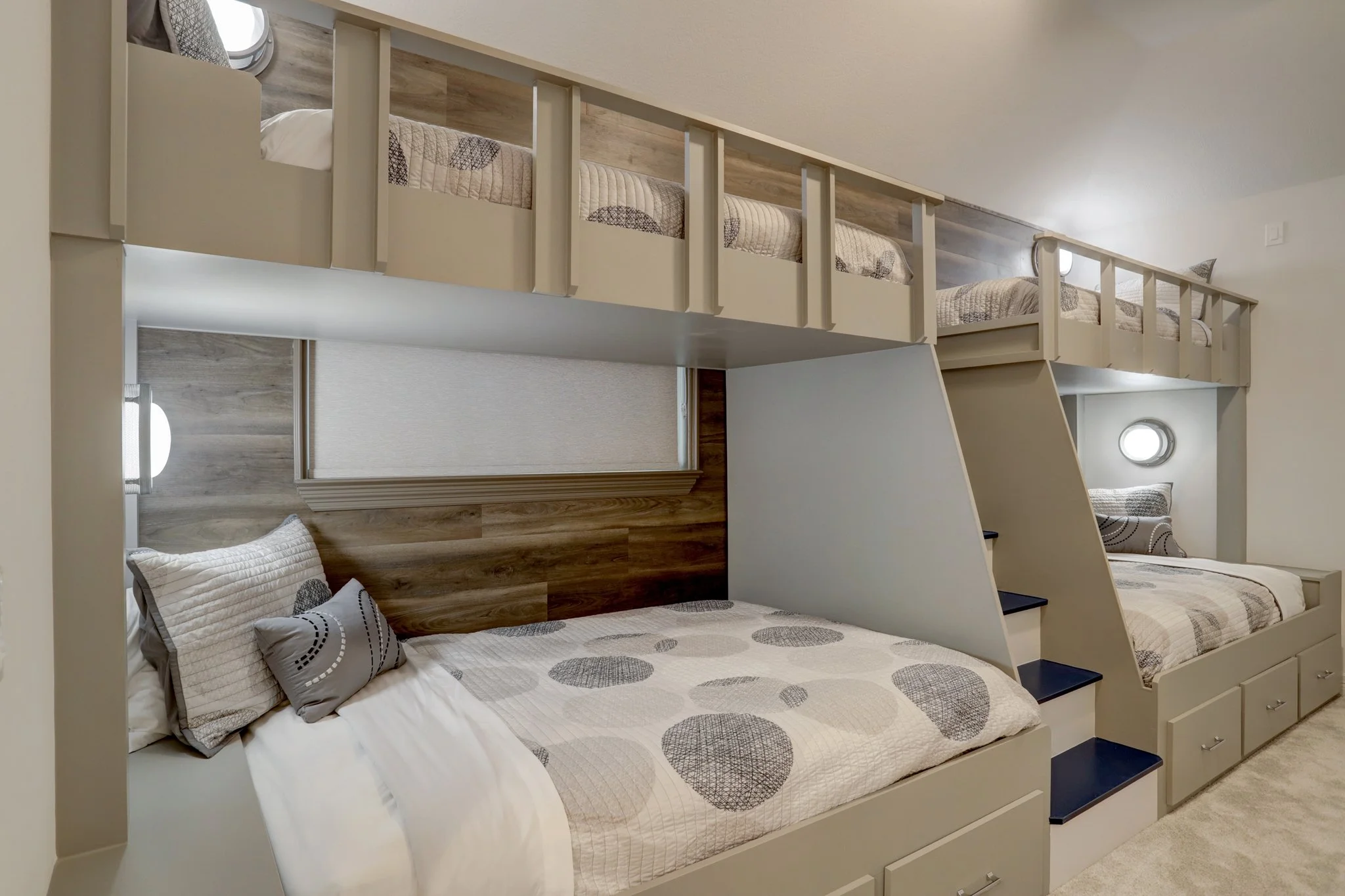 Bedroom with built-in bunk beds, including a lower double bed and two upper single beds, with wooden accents, steps, and storage drawers, illuminated by small wall-mounted lights.