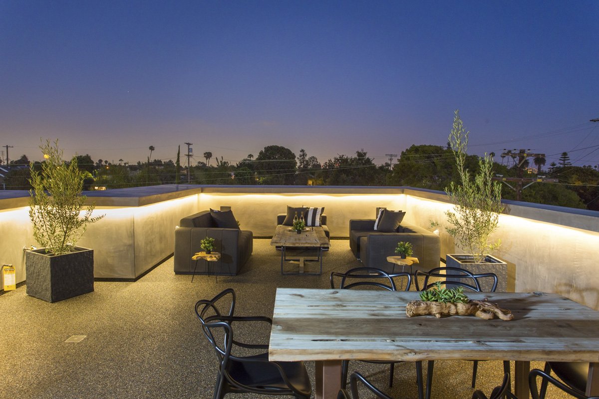Modern rooftop lounge with integrated LED parapet lighting, outdoor sectional seating, and illuminated planters against evening sky.