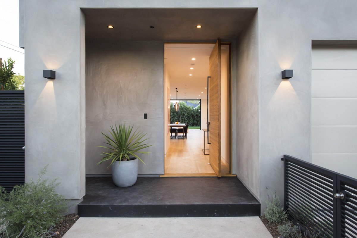 Venice modern entry detail with pivot wood door, recessed soffit lighting, dark concrete landing, and minimalist black metal railing