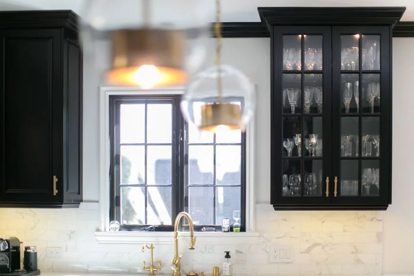 Kitchen window detail with black cabinetry, brass faucet, marble backsplash, and pendant lighting