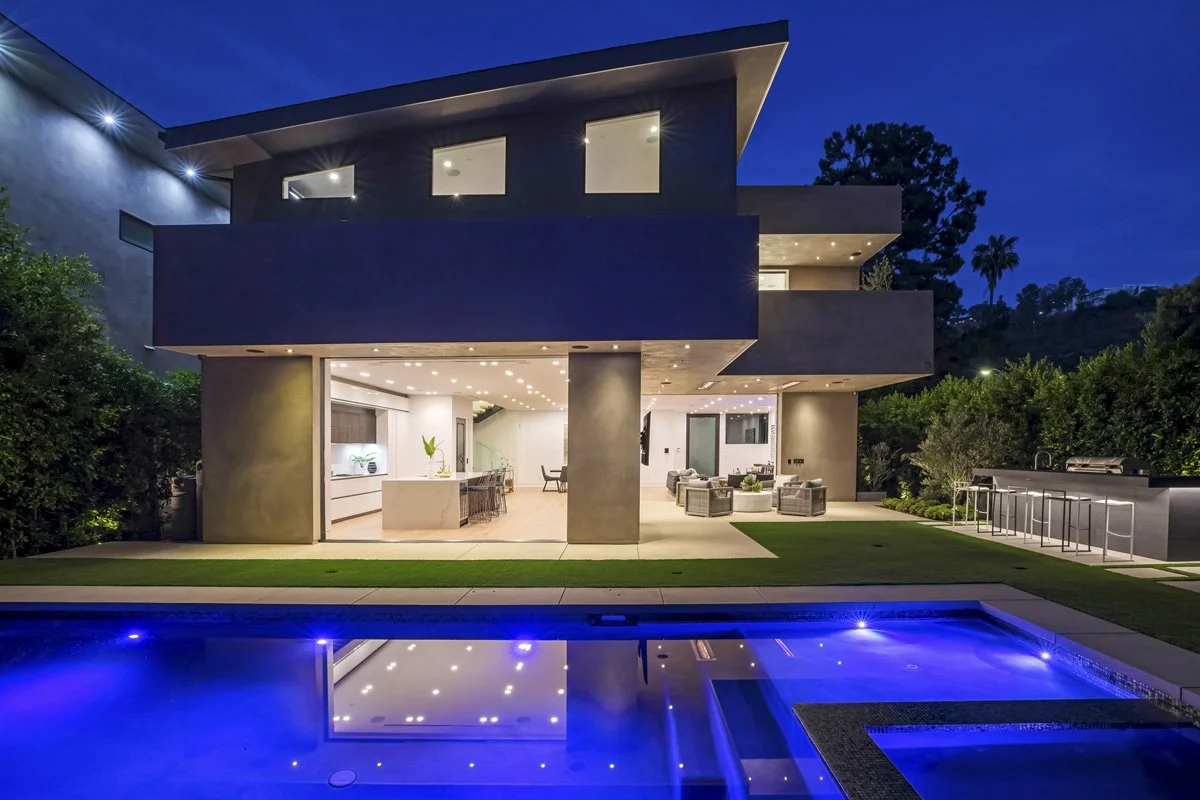 Beverly Hills rear elevation at twilight with sliding glass walls and covered patio lounge