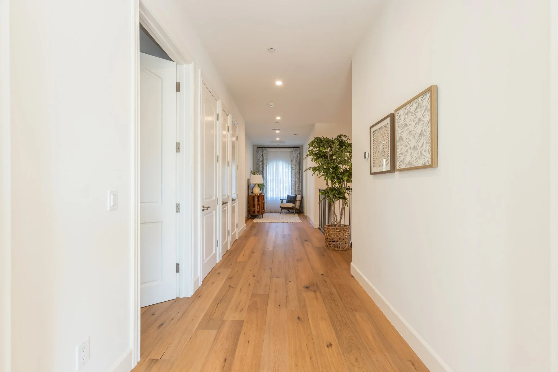 Bright hallway in a custom Brentwood home featuring wide-plank oak flooring, white paneled doors, recessed lighting, and a styled seating nook at the end of the corridor.