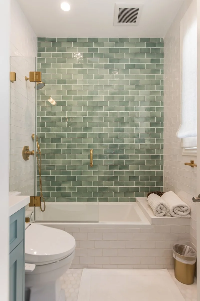 Guest bathroom in a custom Brentwood home featuring a tub-shower with green subway tile accent wall, glass enclosure, brass fixtures, and hex tile flooring.
