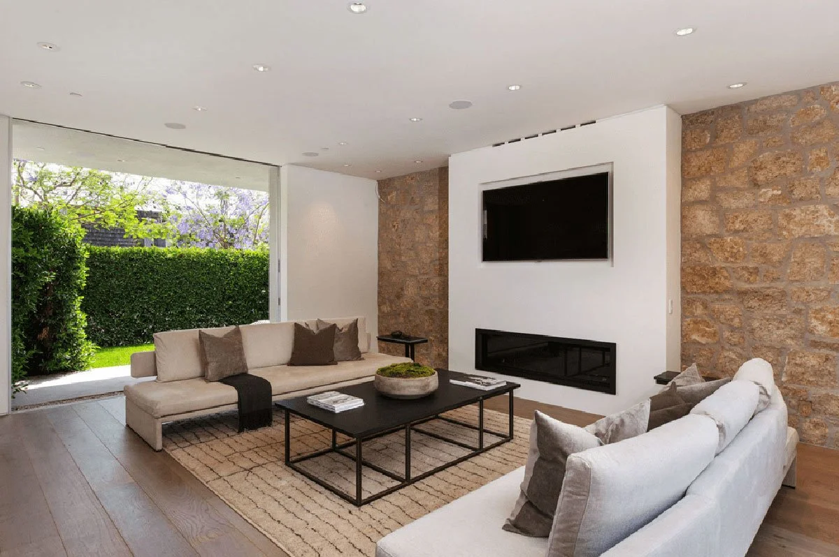 Living room with stone fireplace wall and garden views in West Hollywood custom home.