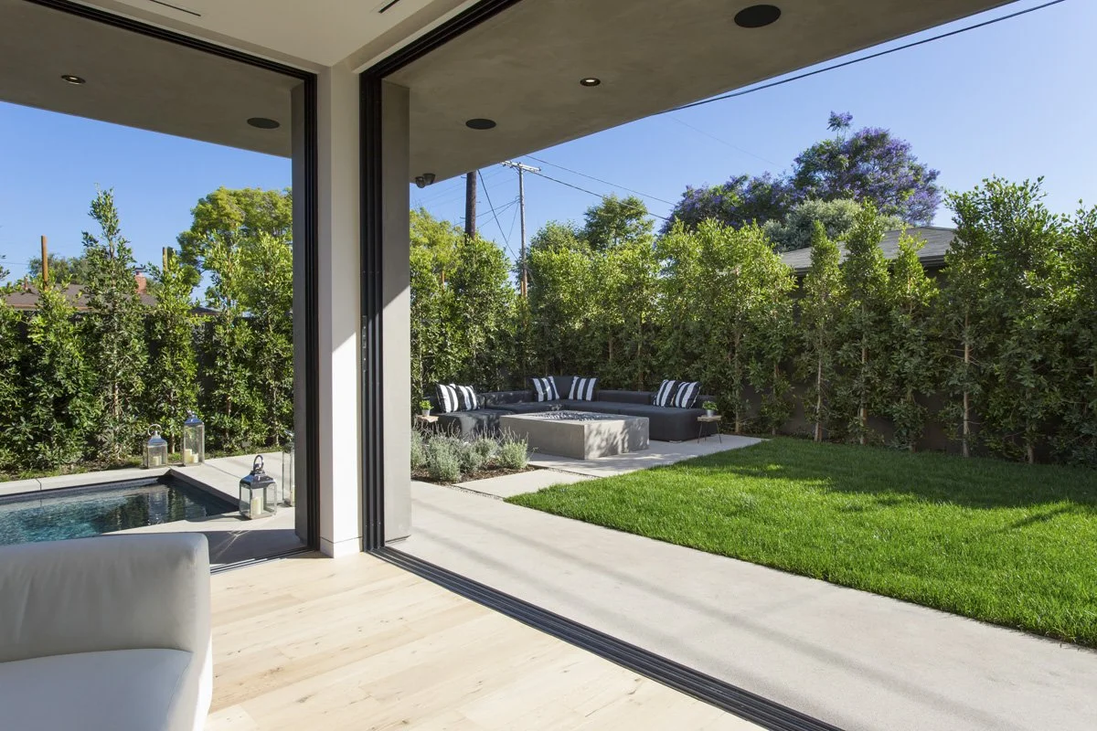 Venice backyard view from interior with expansive sliding glass opening, perimeter hedging, and private lawn