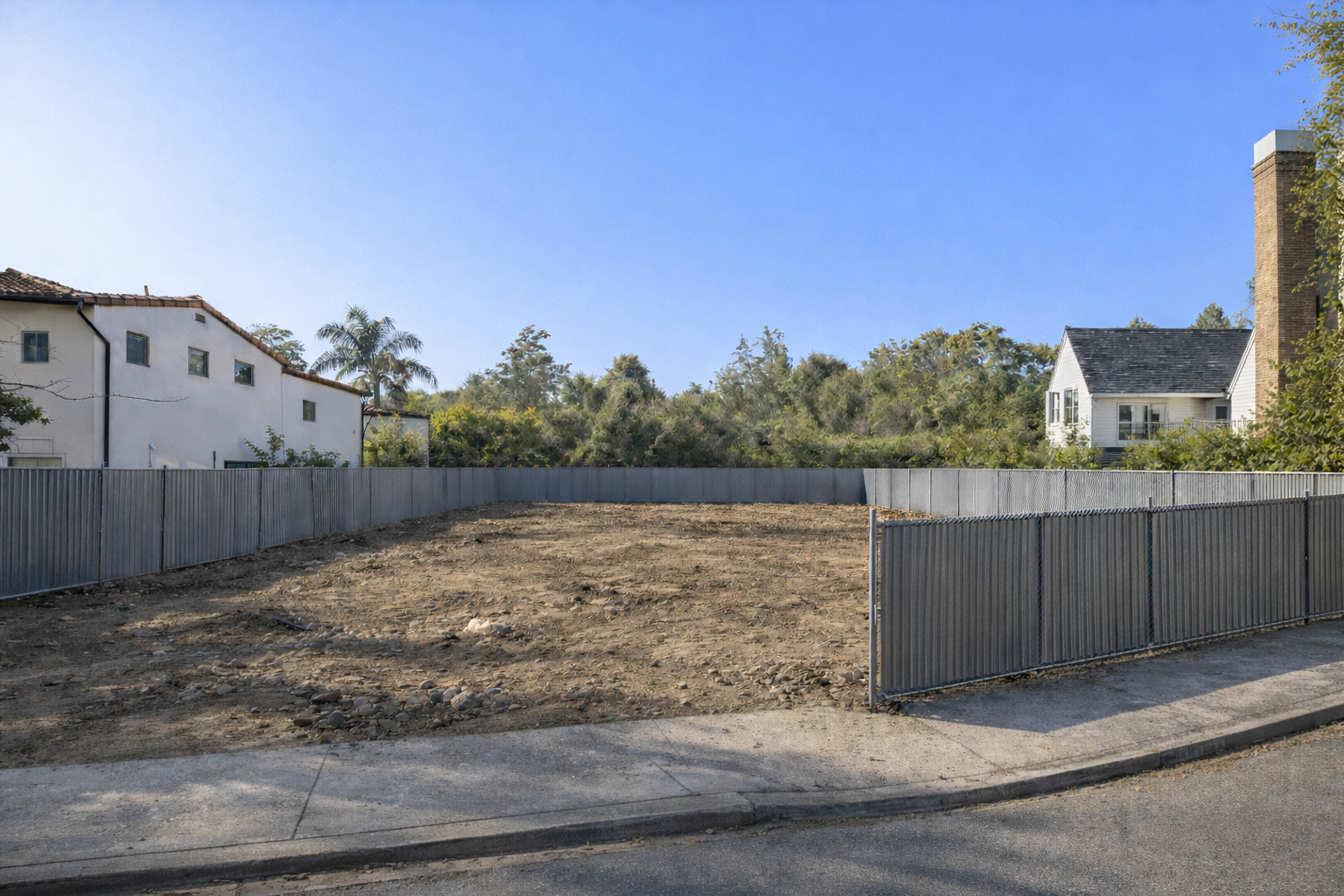 Empty residential lot in Brentwood, Los Angeles prepared for ground-up custom home construction with temporary metal fencing