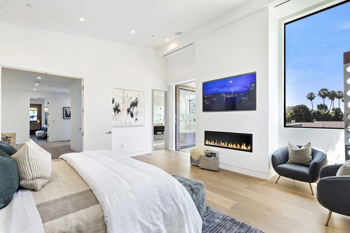 Beverly Hills primary bedroom with wall-mounted television, modern gas fireplace, and floor-to-ceiling window