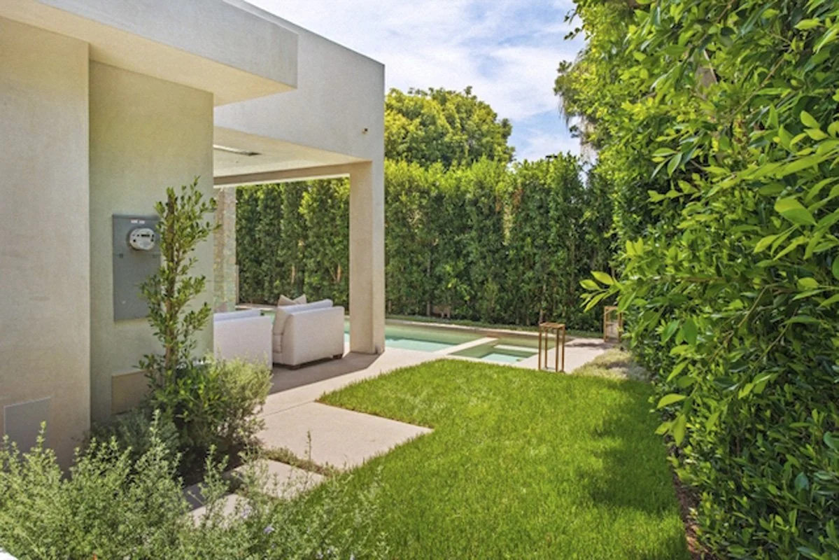 Backyard lawn and covered patio lounge in West Hollywood custom home beside modern swimming pool.