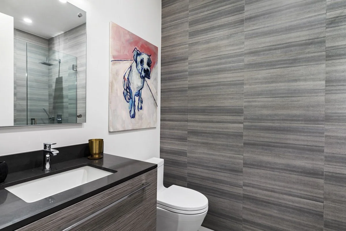 Beverly Hills guest bathroom with stone tile walls, frameless glass shower, and dark quartz countertop