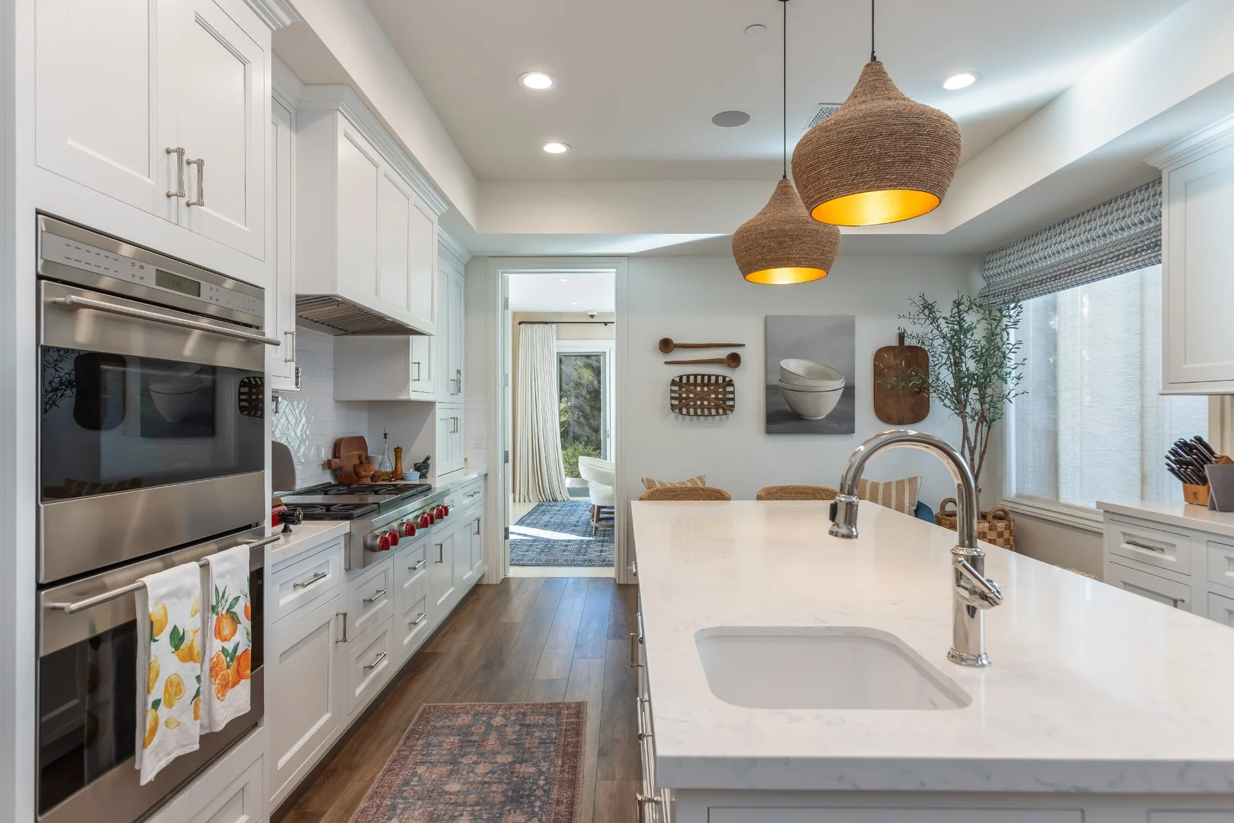 Custom Brentwood kitchen with white shaker cabinetry, marble island countertop, woven pendant lights, stainless steel appliances, and warm wood flooring.