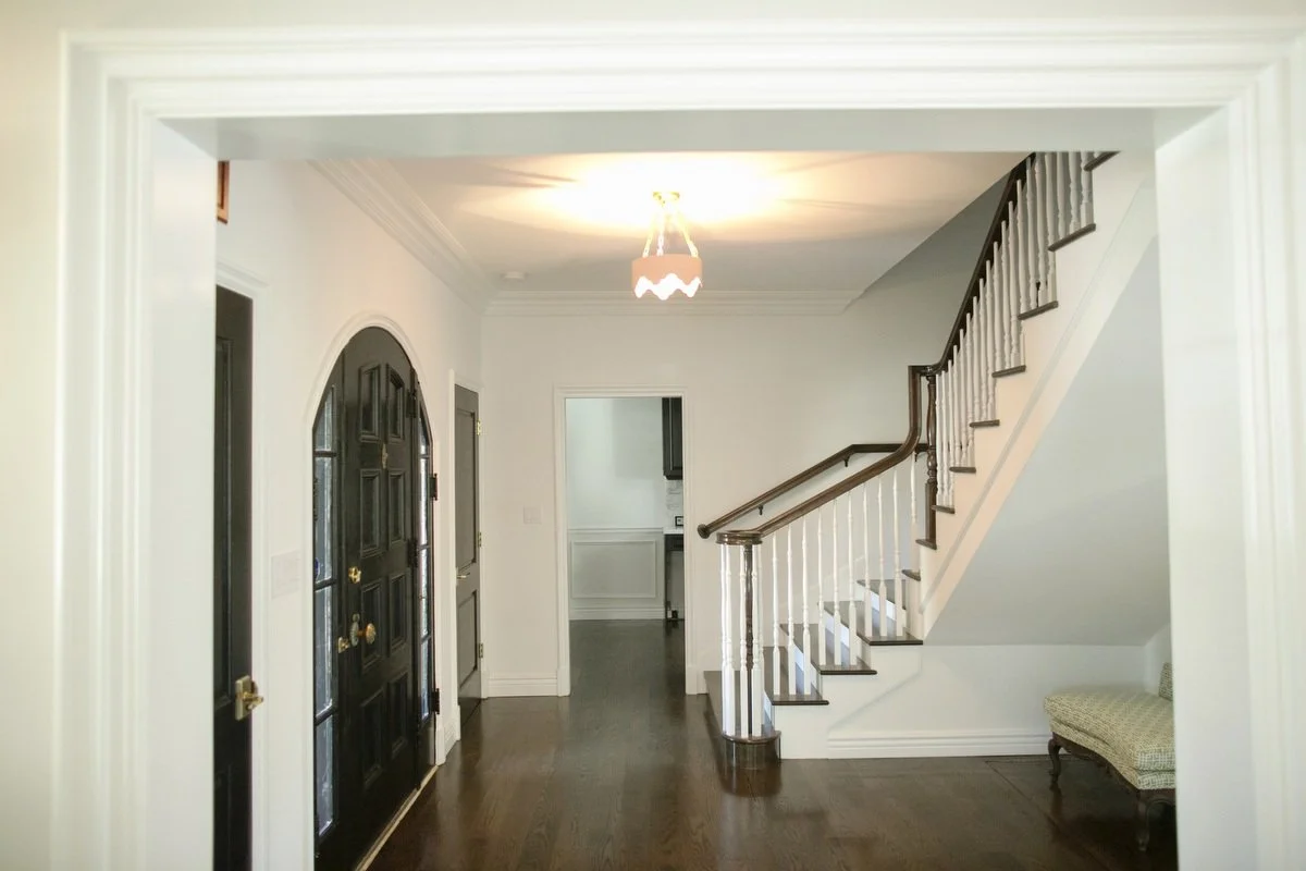 Hancock Park entry hall with dark front door, arched doorway, white staircase railing, and hardwood floors