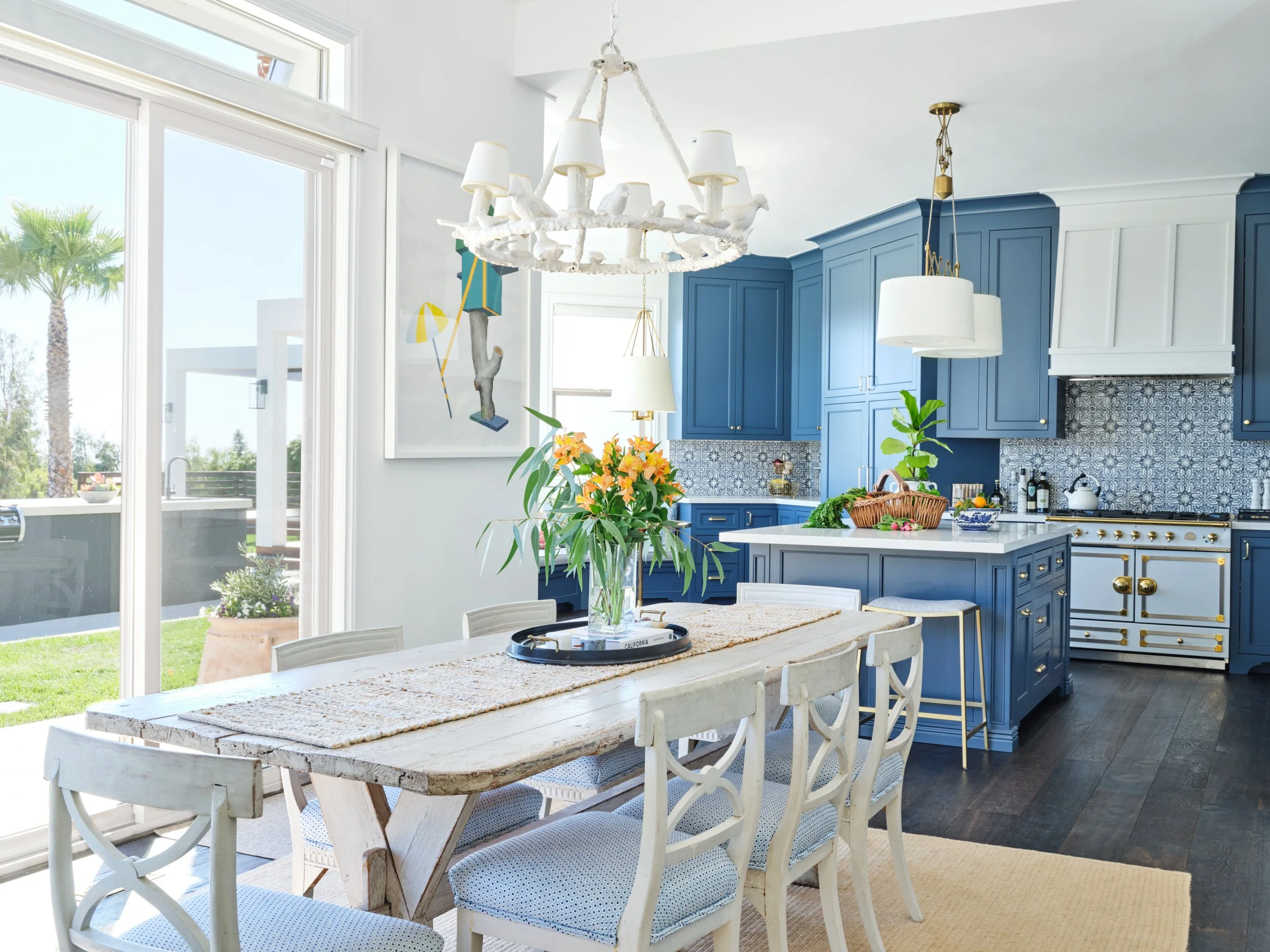 Open-concept Malibu custom home with dining area and blue kitchen cabinetry, large sliding glass doors, indoor-outdoor flow, and garden views by Heart Construction