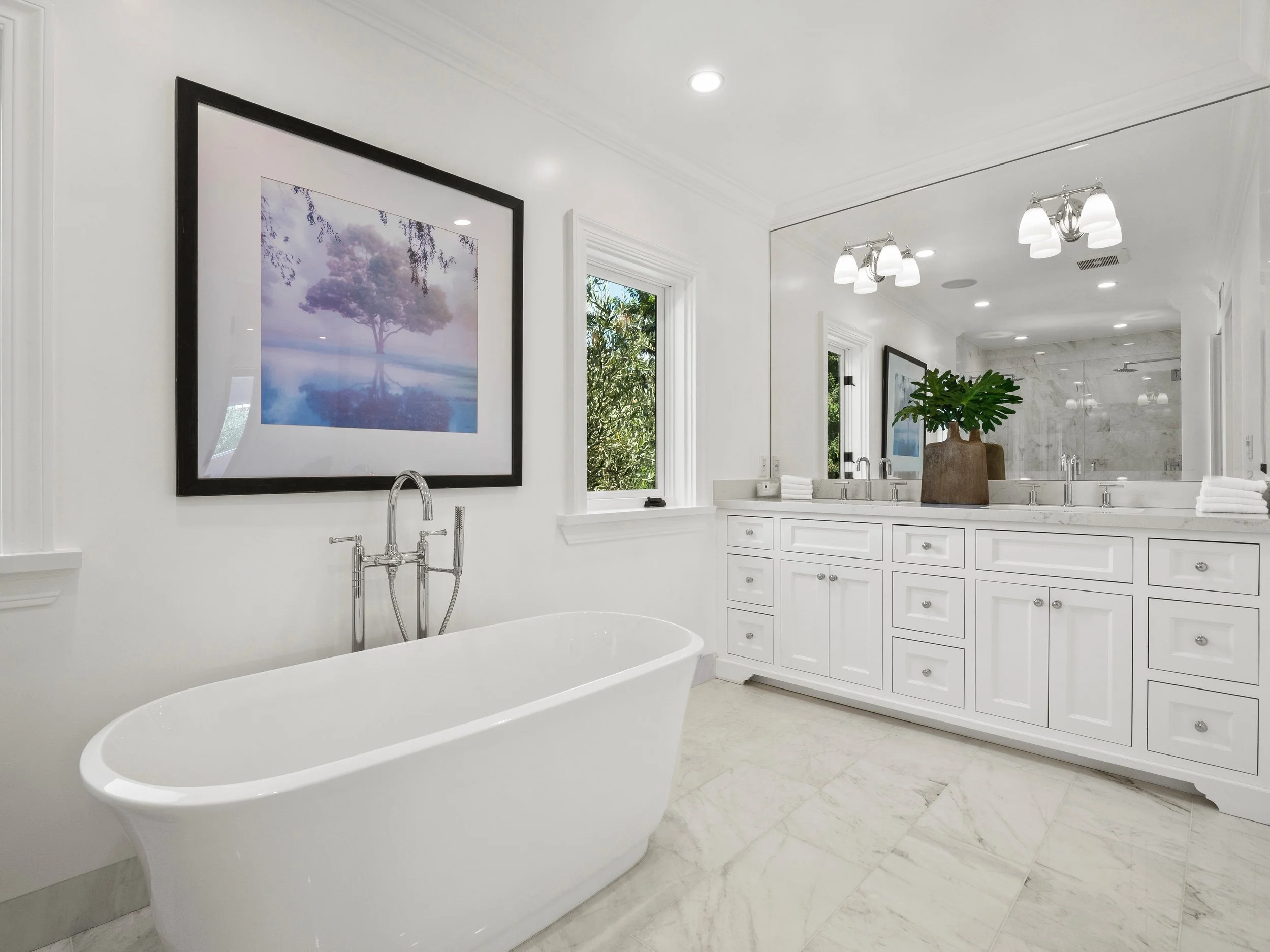 Hancock Park primary bathroom with freestanding soaking tub, double white vanity, marble floors, and glass shower reflected in a full wall mirror.