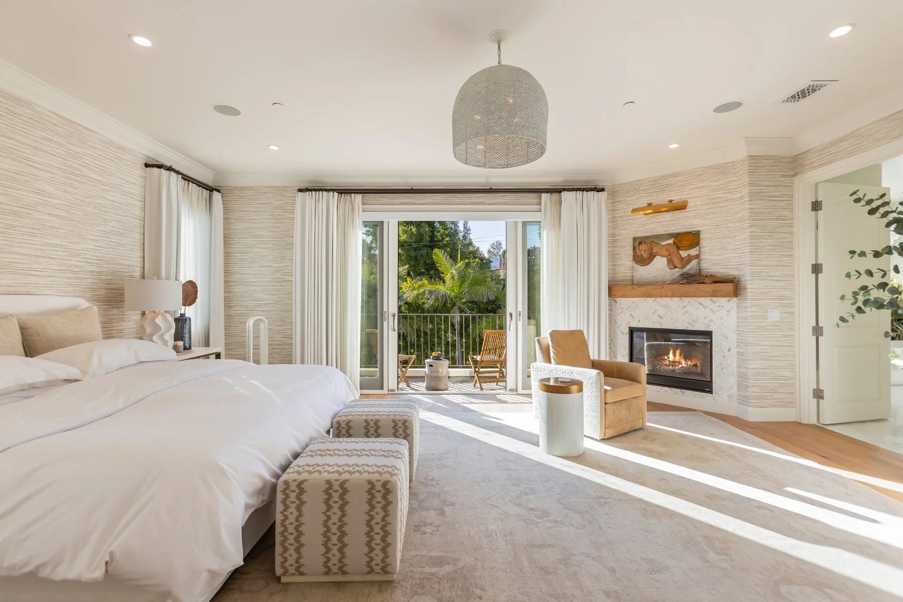 Primary bedroom in a custom Brentwood home featuring a fireplace, private balcony access, soft neutral finishes, and abundant natural light.
