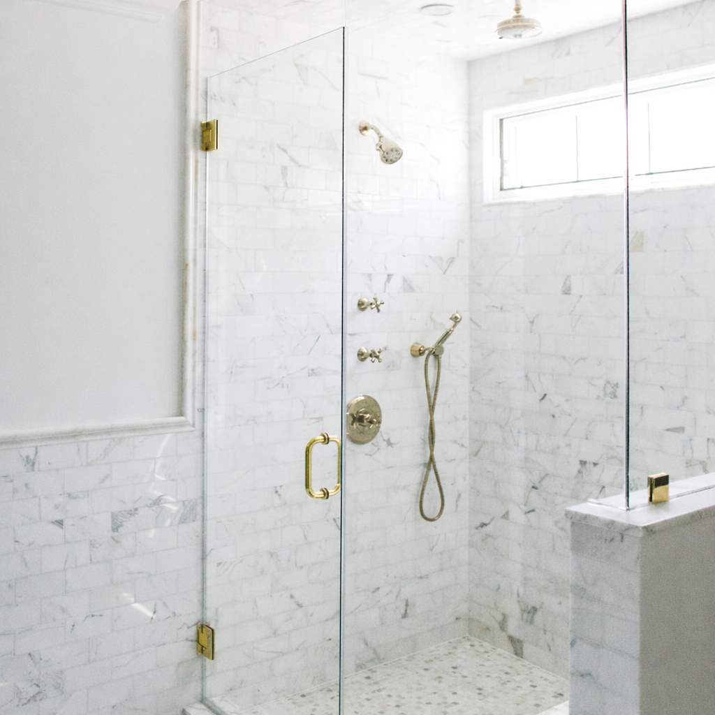 Glass-enclosed marble shower with brass fixtures in a restored Hancock Park Tudor bathroom