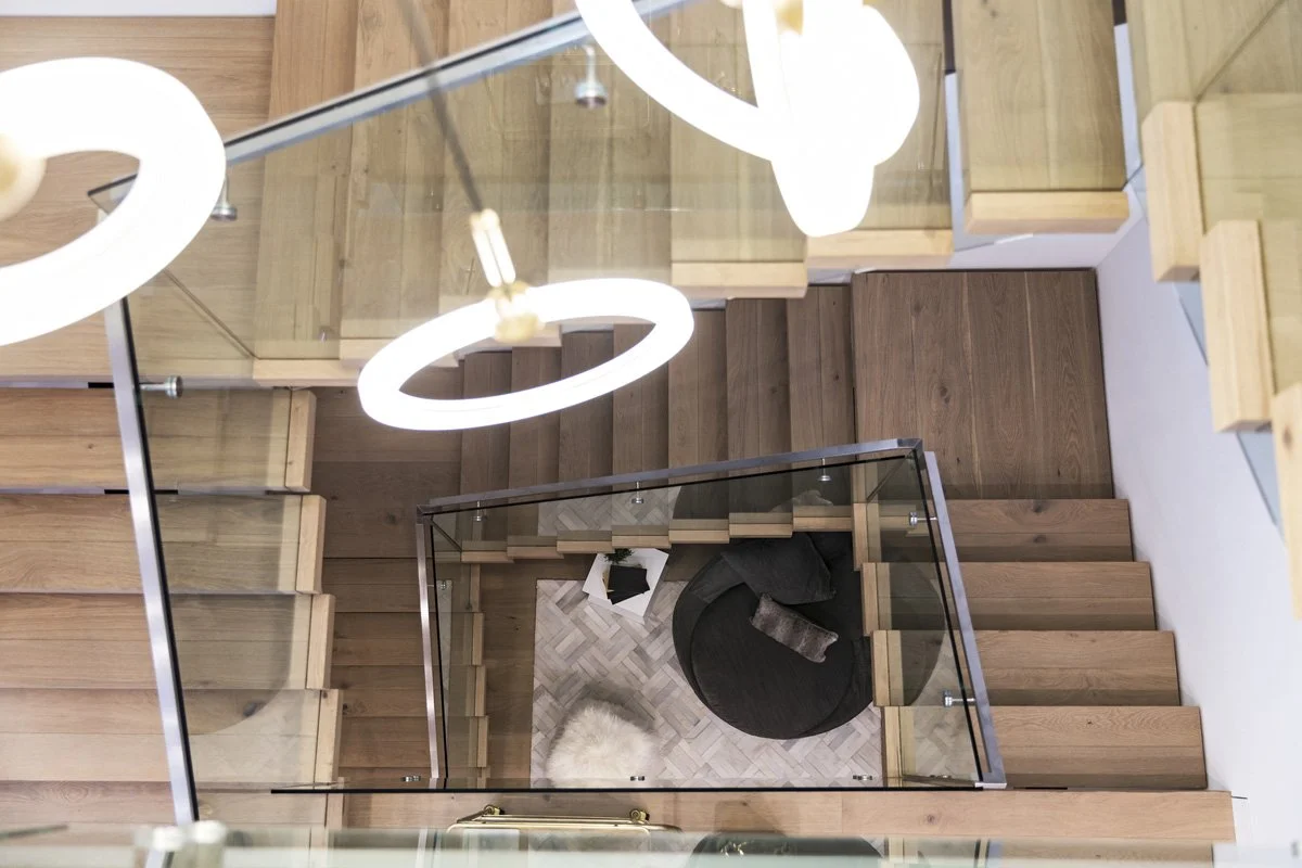 Modern floating wood staircase with glass railing and sculptural pendant lights in a Calabasas luxury home by Heart Construction