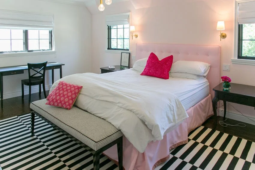 Bedroom with upholstered pink headboard, brass sconces, and striped rug in Hancock Park remodel
