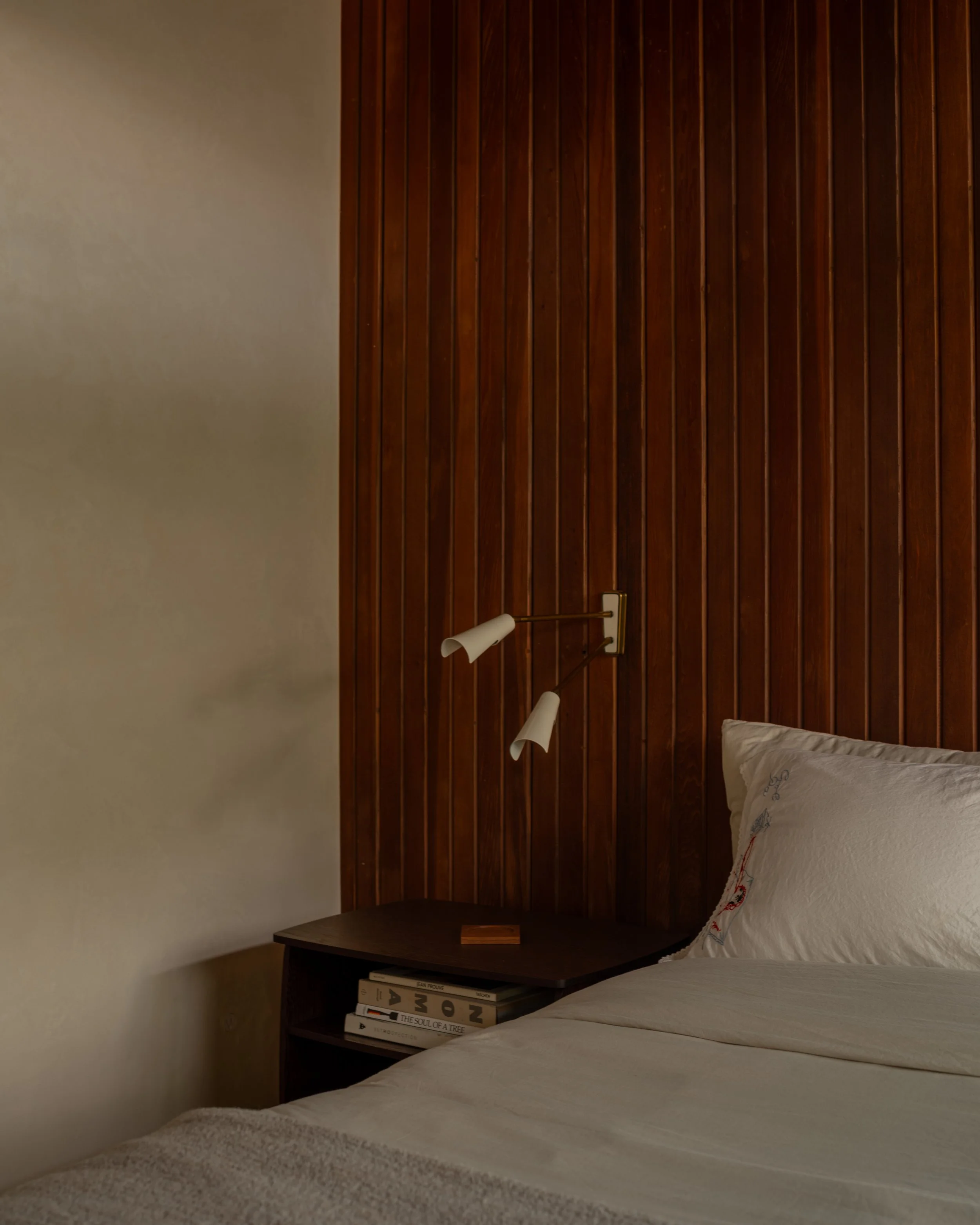La Cuesta bedroom detail with vertical walnut panel wall, built-in nightstand, and modern brass wall sconce.