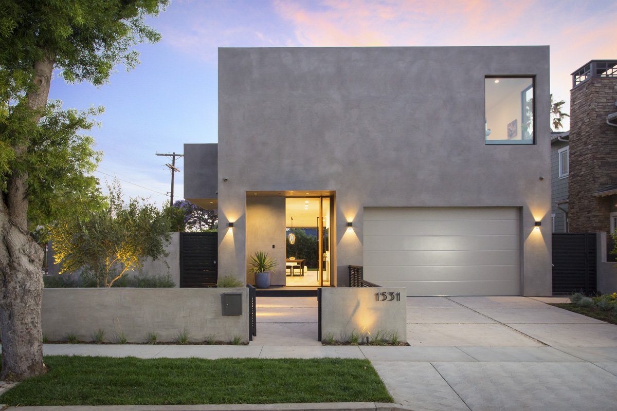 Venice modern custom home front elevation at dusk with smooth plaster façade, recessed wood entry, integrated wall sconces, and minimalist concrete driveway