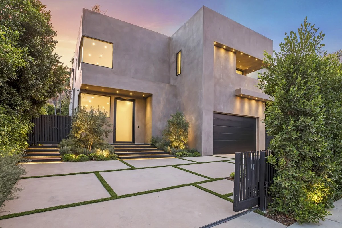 Modern Beverly Hills custom home with smooth stucco exterior, architectural driveway with grass inlays, and illuminated entry at dusk.